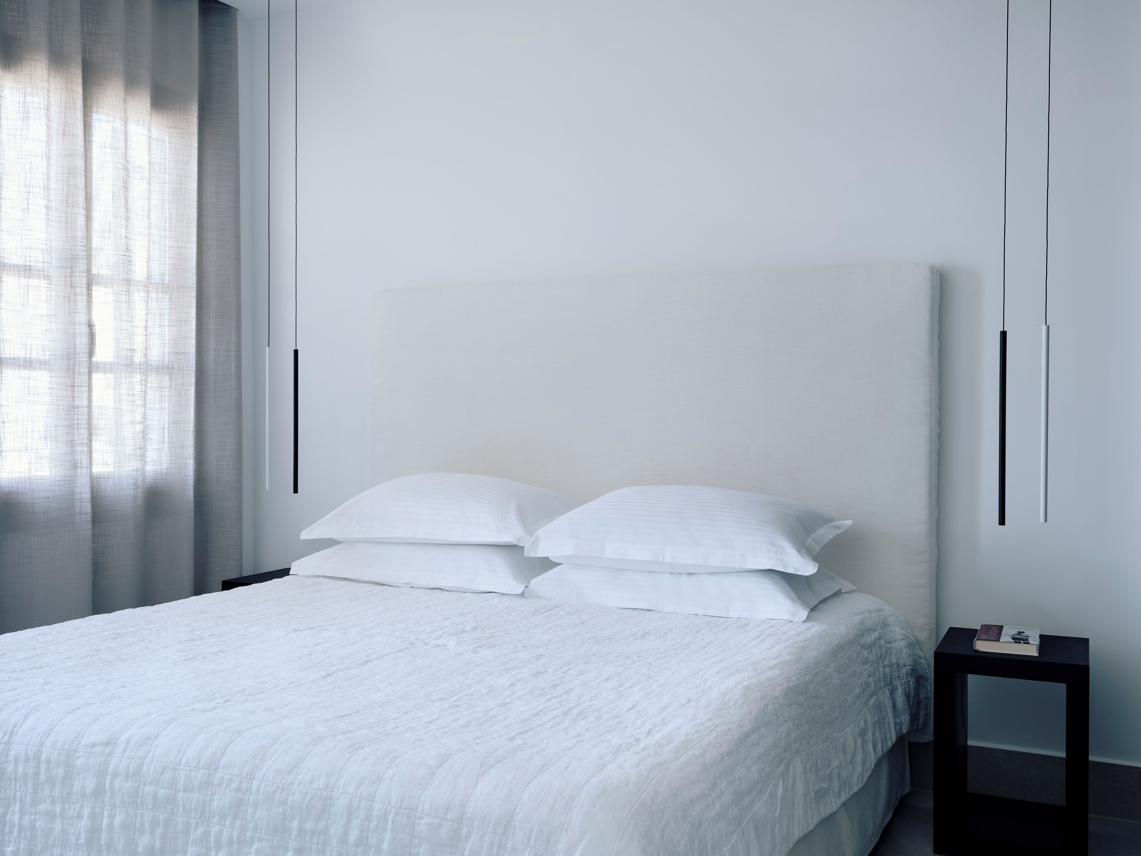 A modern bedroom with a large bed, white bedding, and a small bedside table with a book.