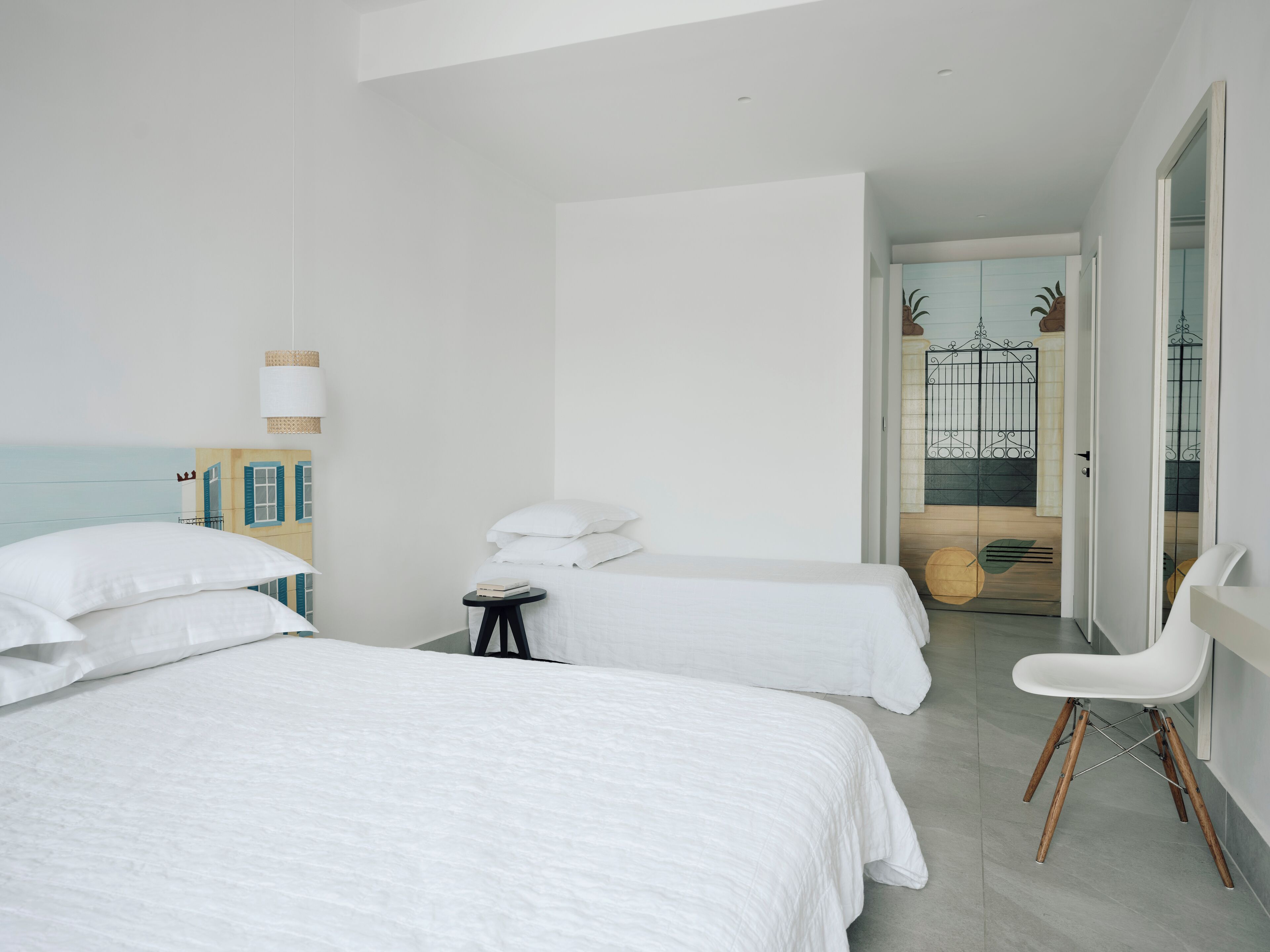 A hotel room with two beds, a small table, a chair, and a view of the outside balcony.