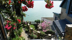 Een balkon met een hek dat uitkijkt op een wateroppervlak, omringd door weelderige begroeiing en bloeiende planten.