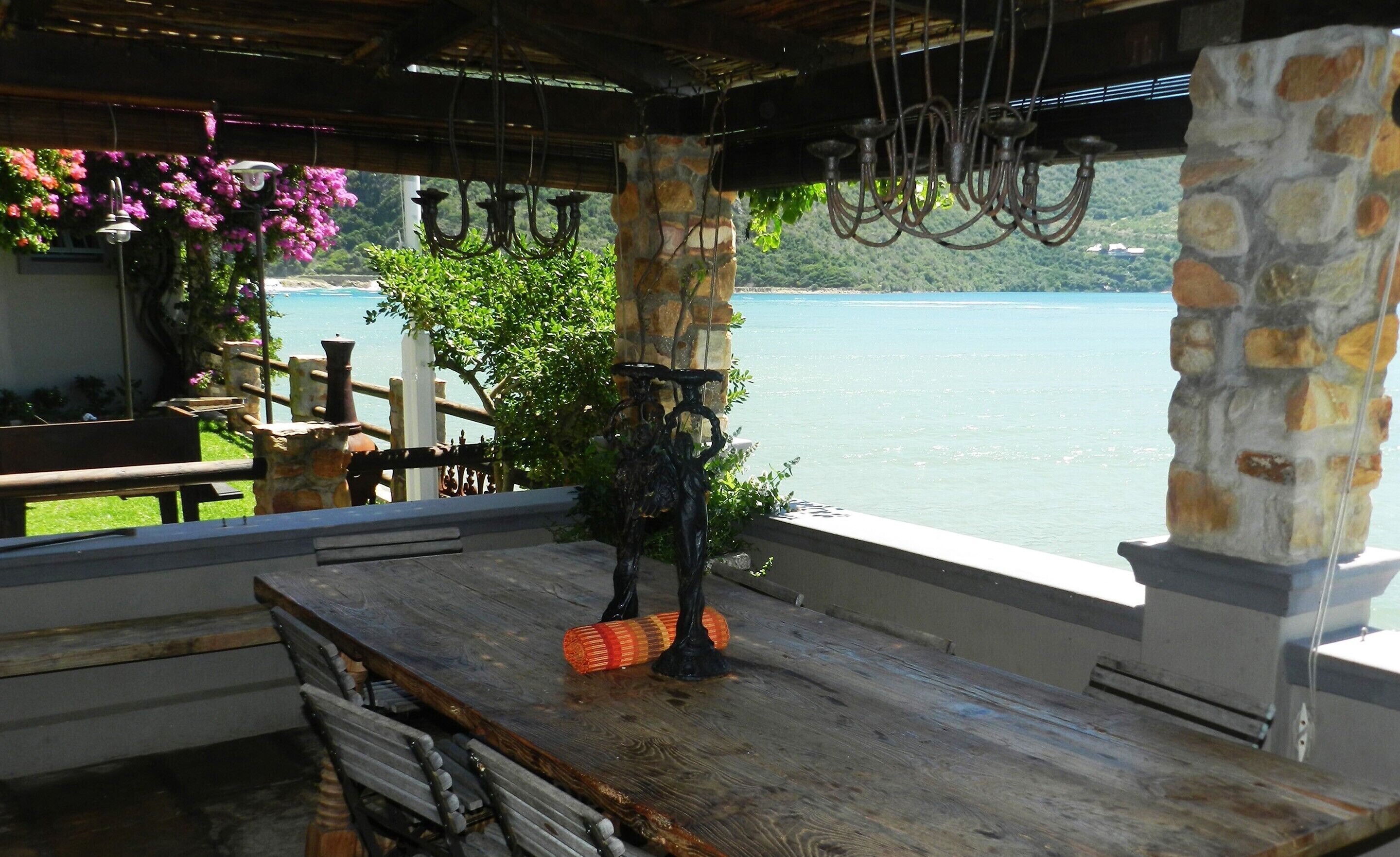 A rustic outdoor seating area with a stone pillar, wooden table, and benches overlooking a lake.