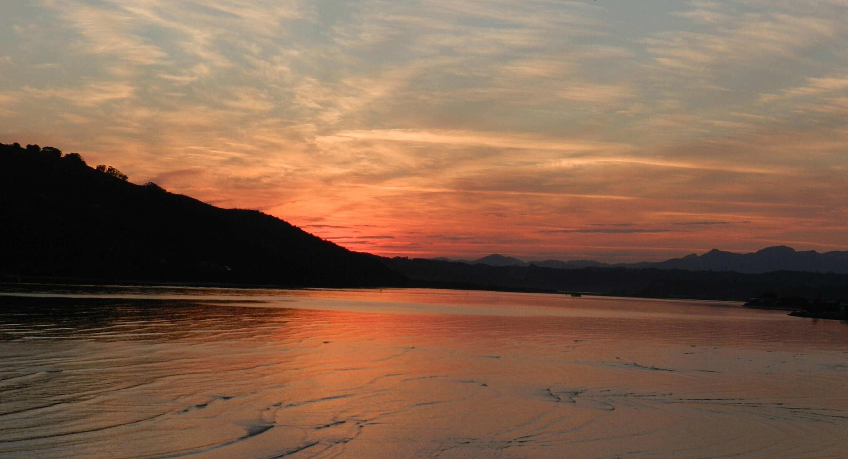 Een zonsondergang boven een rustig meer met bergen op de achtergrond.
