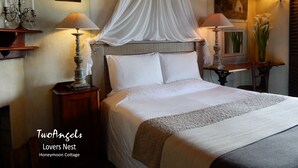 Een keurig opgeruimde slaapkamer met een hemelbed, bedlampen, een ingelijst plaatje en een spiegel.