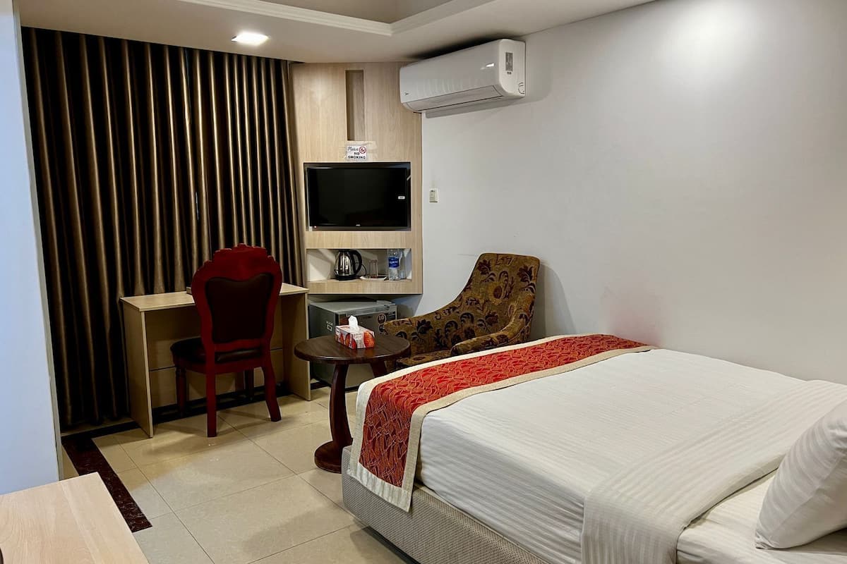 A hotel room with a bed, a desk with a chair, a television, and an air conditioning unit.