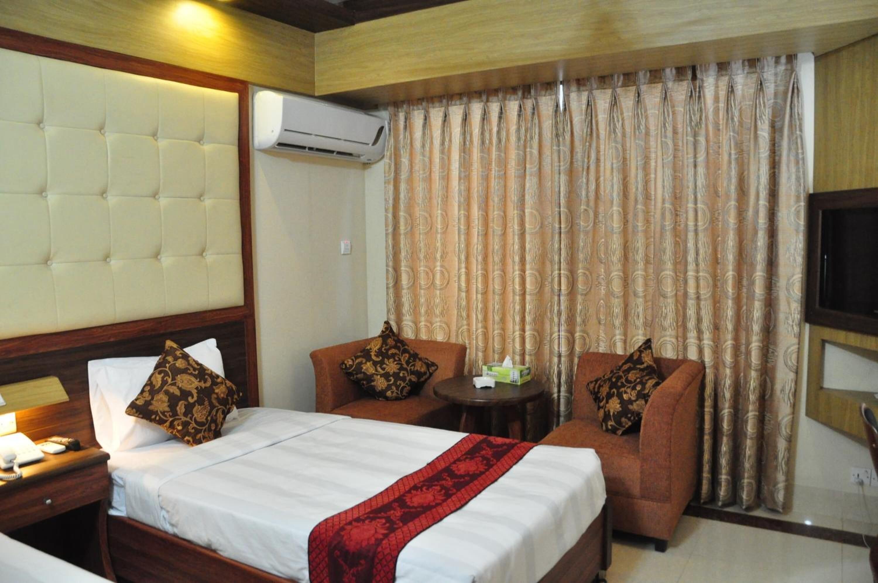 Una habitación de hotel con una cama, dos sillones, una mesita y un televisor.