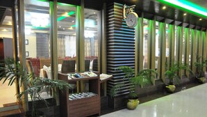 Een hotel lobby met een receptiebalie, een klok en kamerplanten.
