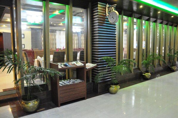 A hotel lobby with a reception desk, a clock, and potted plants.