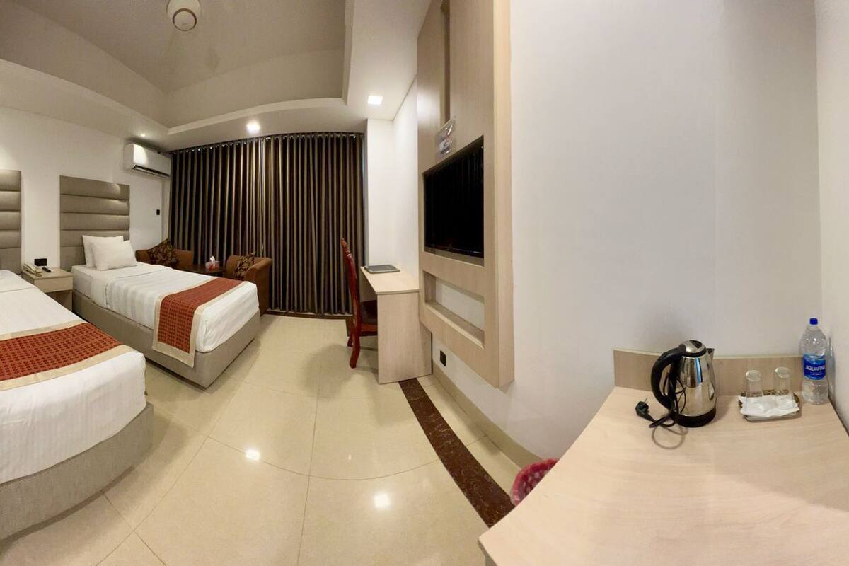 A hotel room with two beds, a TV, a desk with a kettle, and a water bottle.
