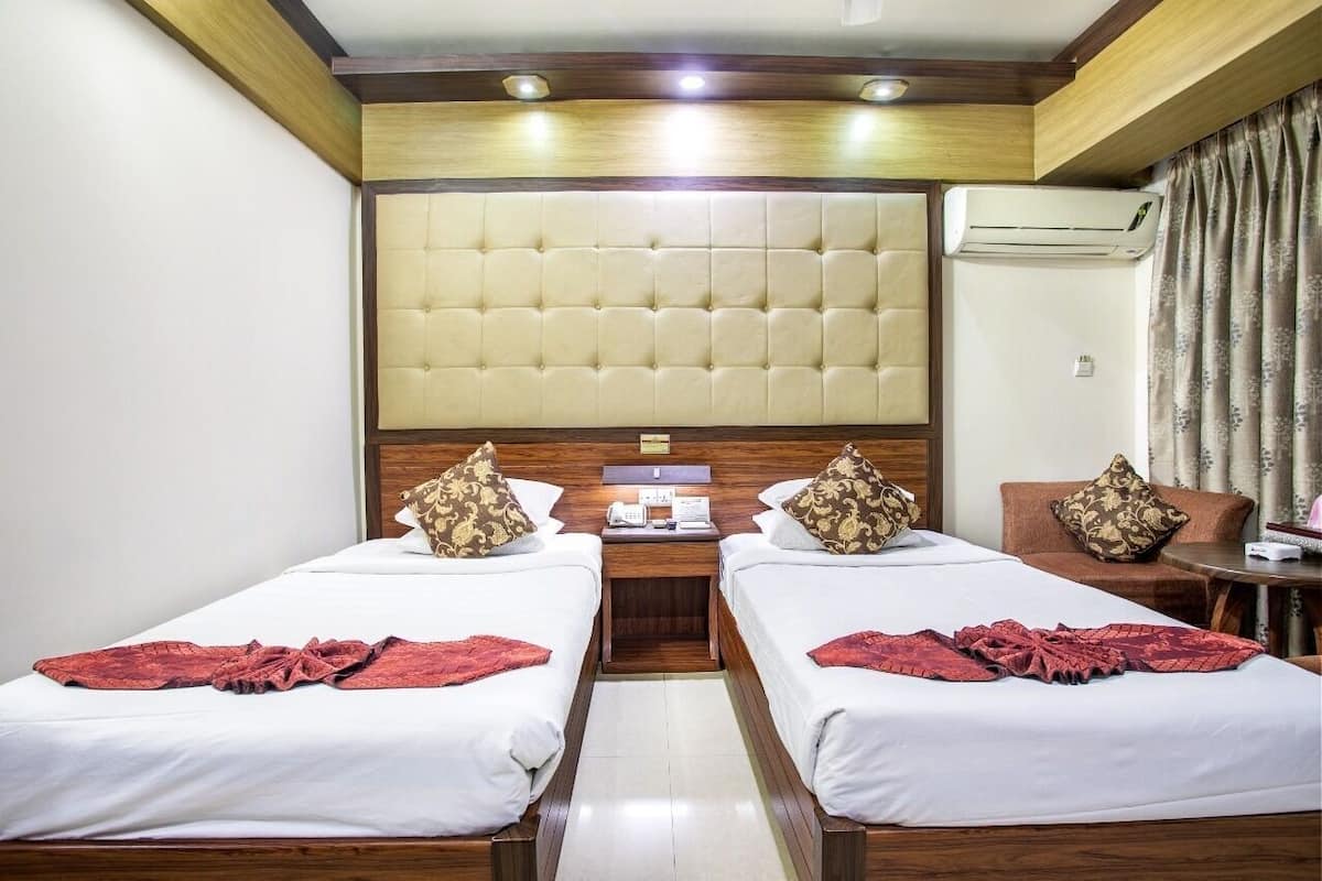 A hotel room with two beds, a large padded headboard, an air conditioning unit, a small table, and a chair.