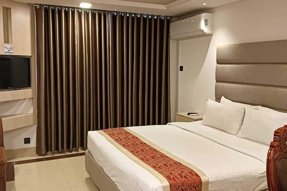 A hotel room with a bed, a TV mounted on the wall, a desk, and a chair.