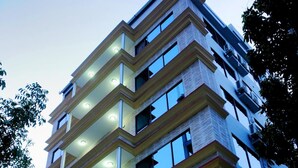 Een meerlaags hotel met een modern ontwerp, met balkons op elke verdieping, grote ramen en een goed verlichte entree.
