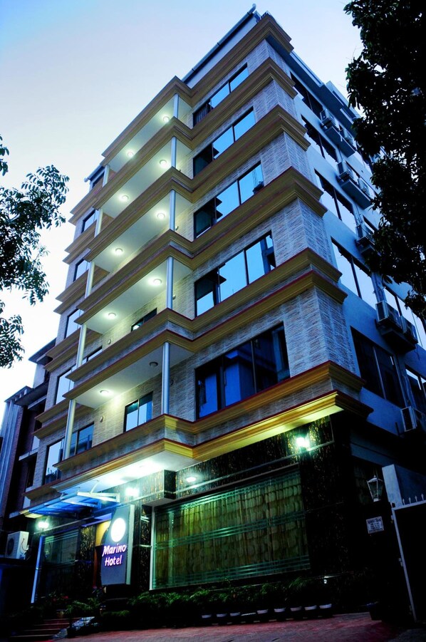 A multi-story hotel with a modern design, featuring balconies on each floor, large windows, and a well-lit entrance.