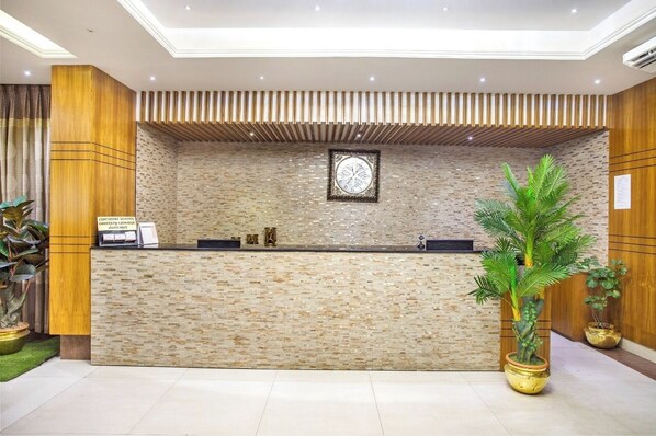 A reception desk with a stone wall backdrop, a clock, and potted plants. - Marino Hotel Uttara (Dhaka)