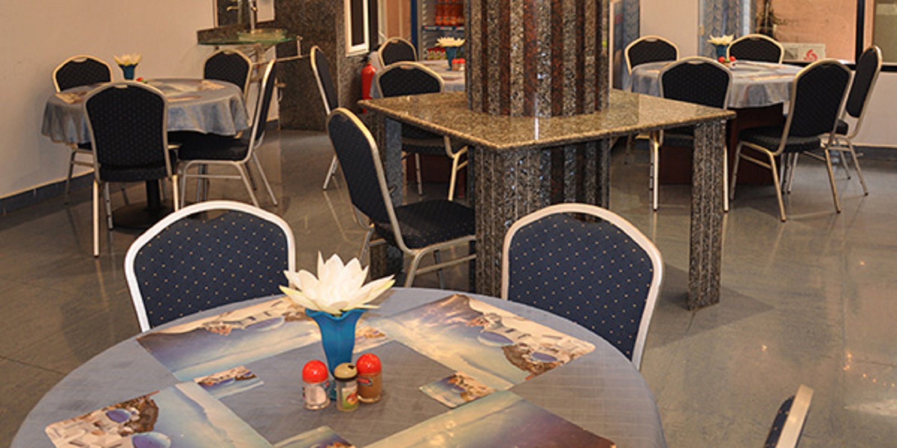 A restaurant with round tables, blue chairs, and a central decorative vase.