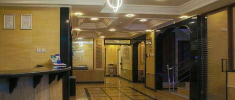 A hotel lobby with a reception desk, a staircase, and a tiled floor.