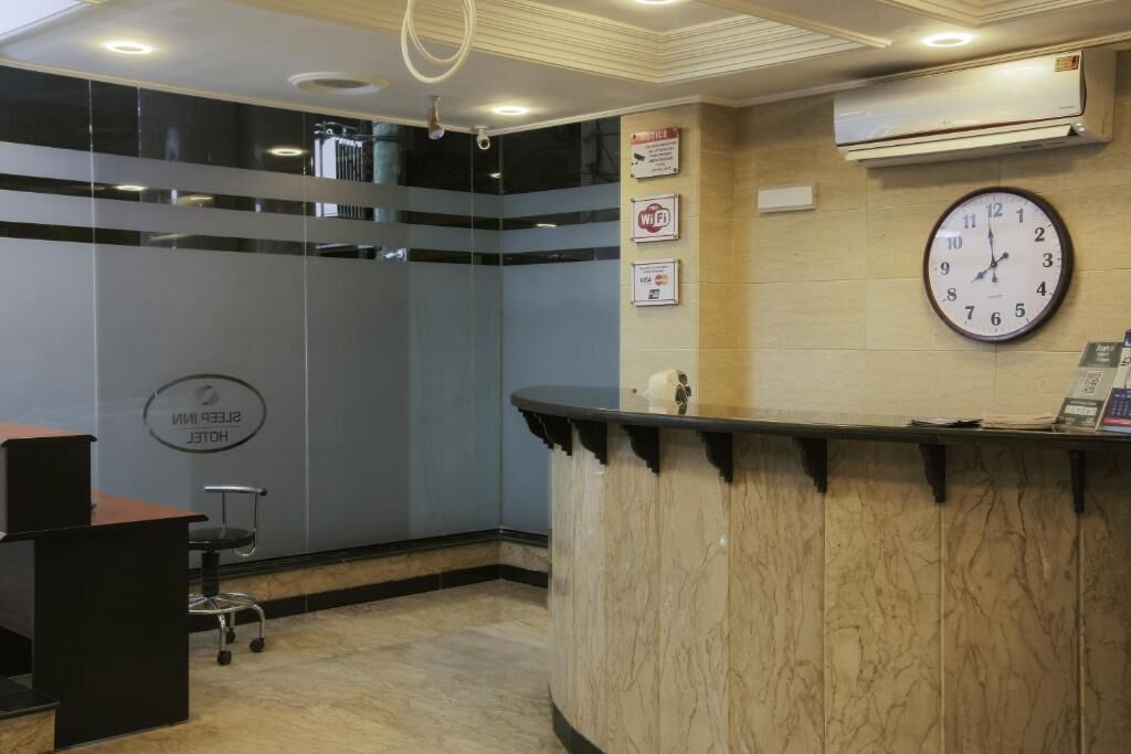 Zona de recepción de un hotel con mostrador de mármol, un reloj y un cartel que indica la disponibilidad de Wi-Fi.