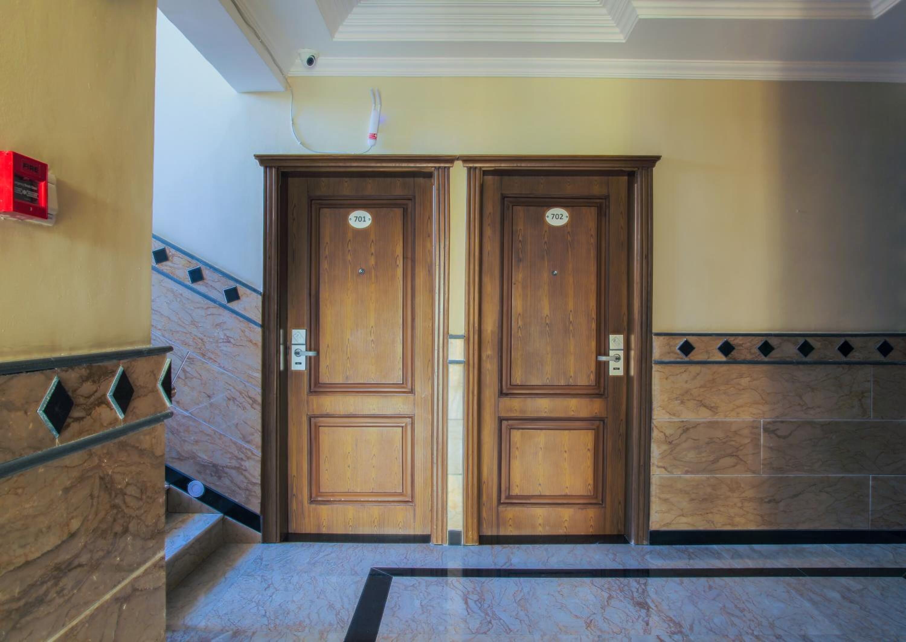 A double wooden door with numbers 701 and 702, a marble staircase, and a fire alarm on the wall.