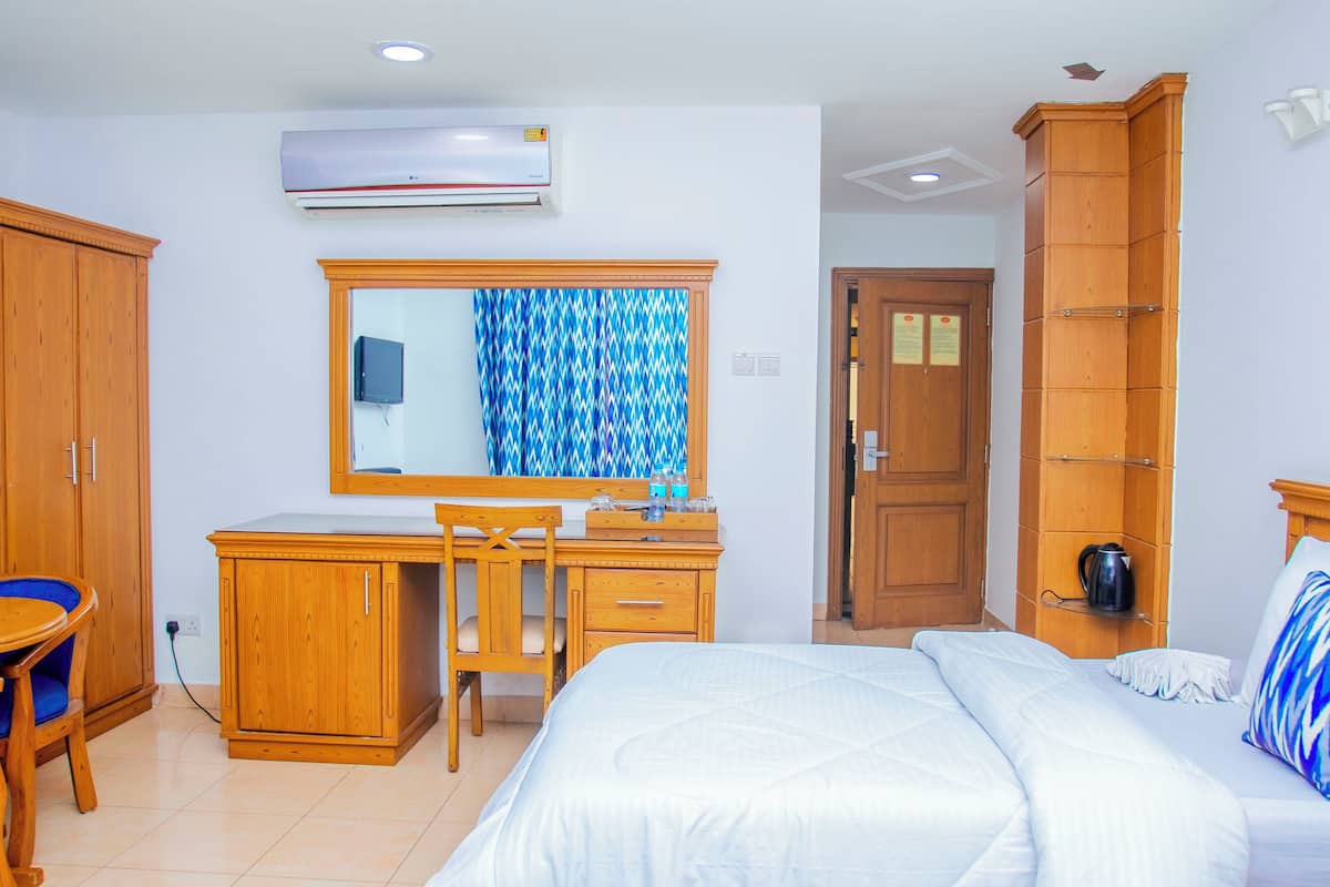 Una habitación de hotel con una cama, un escritorio con una silla, un armario y la puerta del baño.