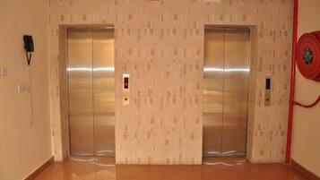 A hallway with two elevators, a wall-mounted phone, and a red fire hose.
