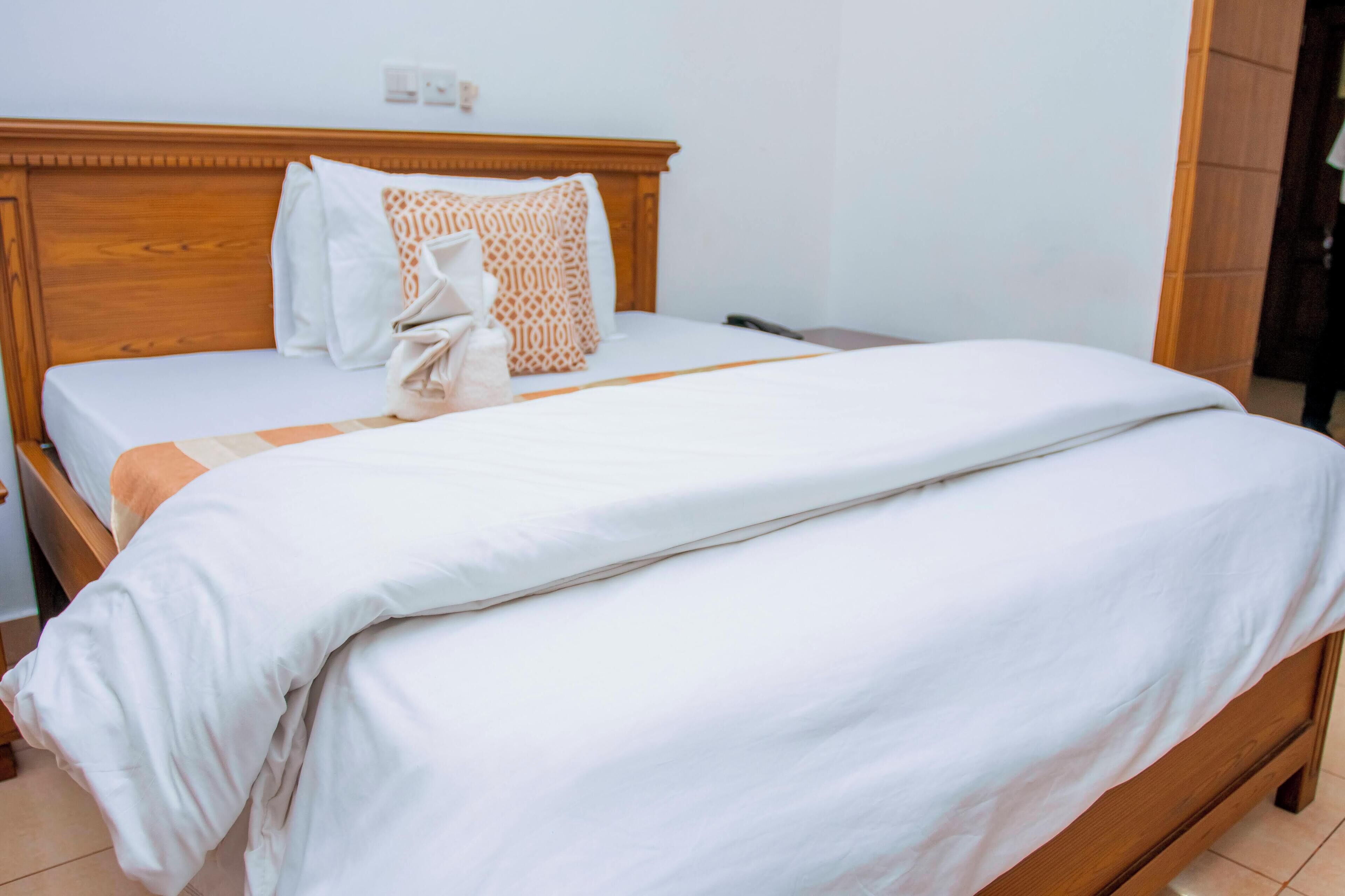 Cama bem arrumada com cabeceira de madeira, roupa de cama branca e almofada decorativa estampada.