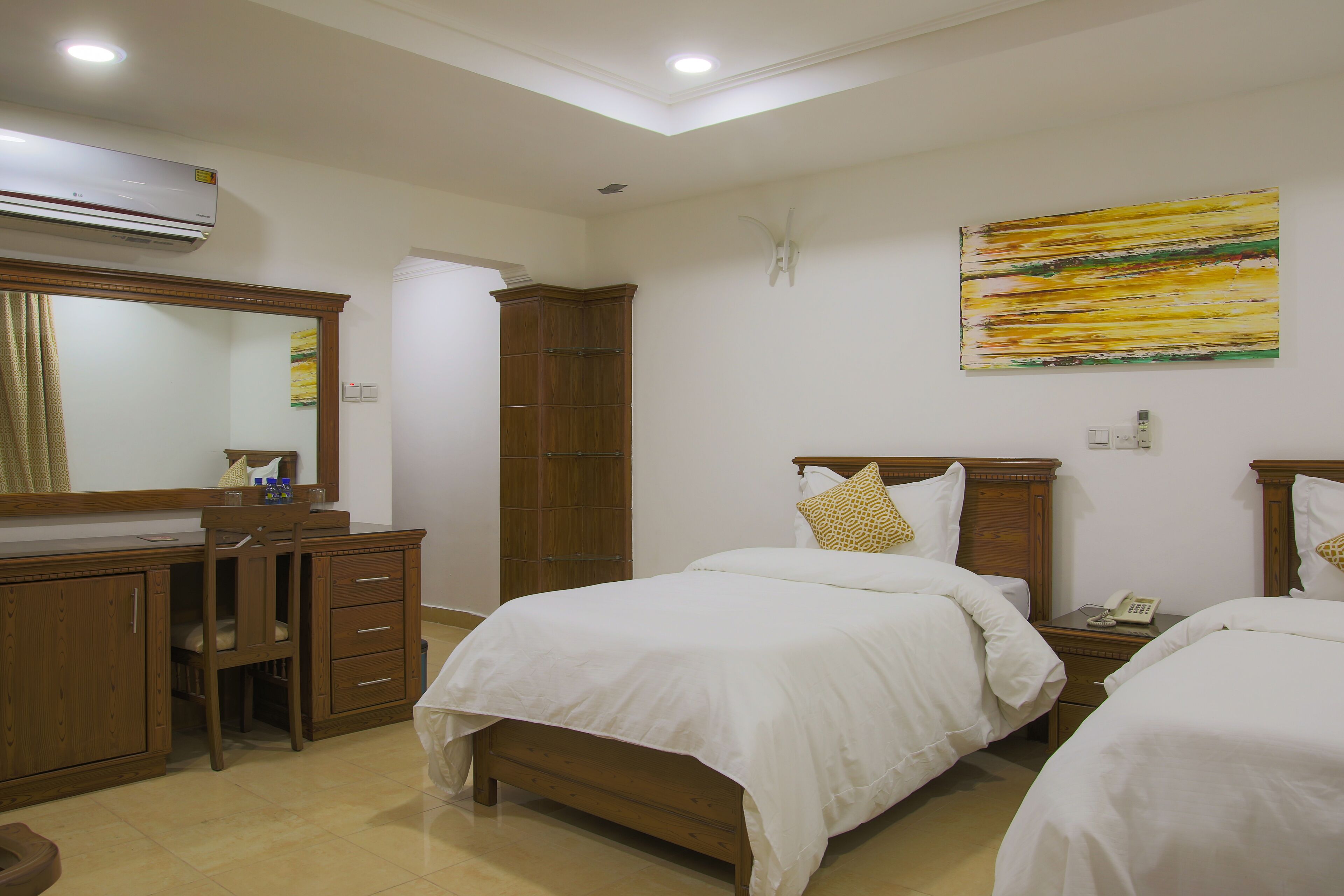 Habitación de hotel con dos camas, un escritorio de madera, un armario y un espejo grande.