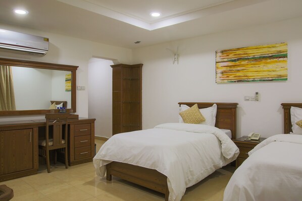 A hotel room with two beds, a wooden desk, a wardrobe, and a large mirror.