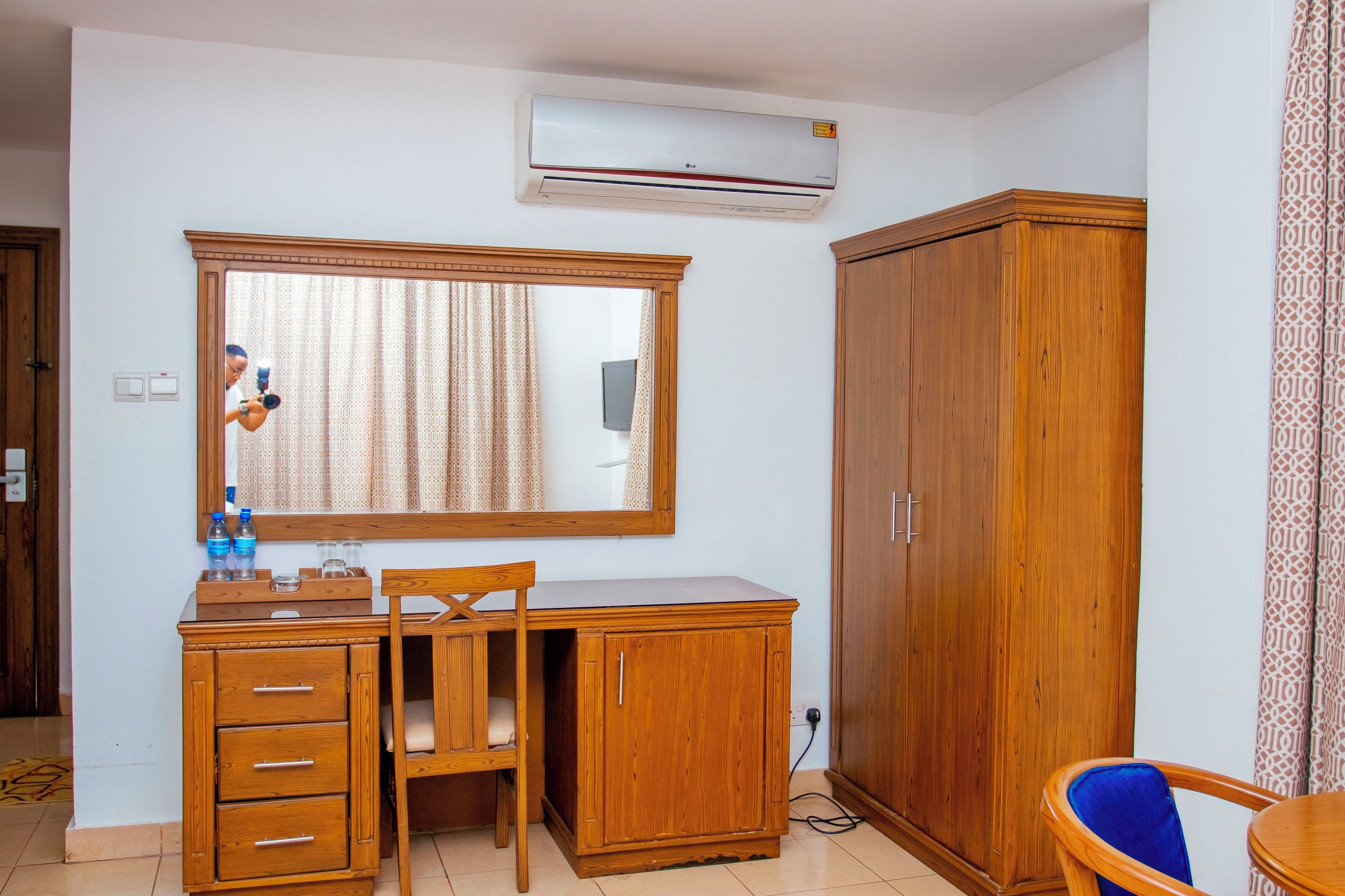 Una habitación con un escritorio de madera, una silla, un armario, un espejo y un equipo de aire acondicionado.