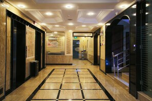 A hotel lobby with a marble floor, a reception desk, and an elevator.