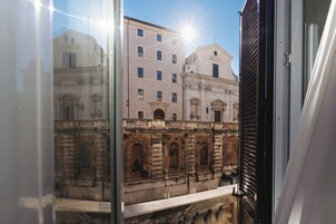 A view through a window of a building with classical architecture, featuring arched windows and a balcony.