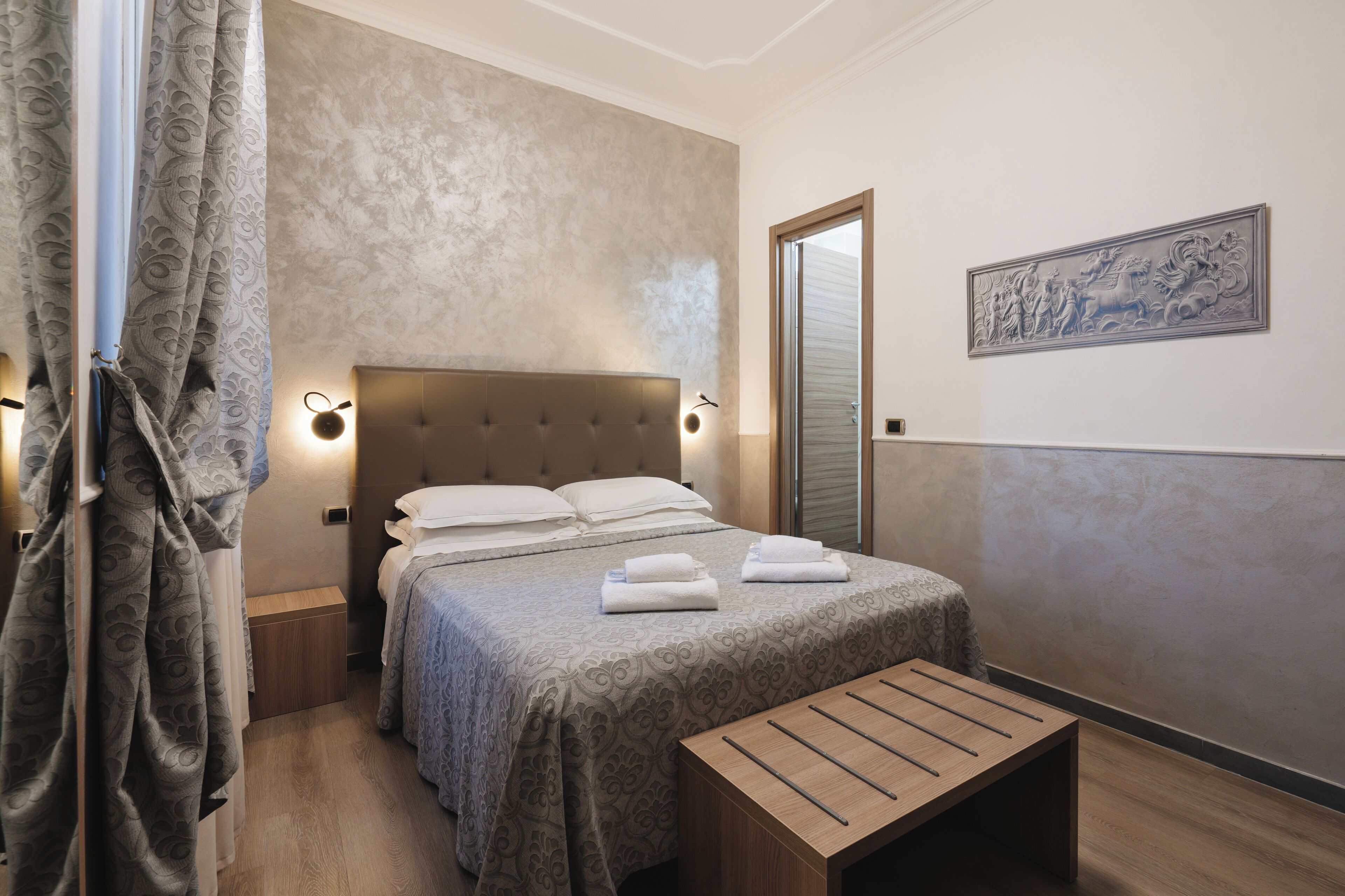 A neatly arranged bedroom with a bed, bedside tables, a bench, and a wall-mounted artwork.