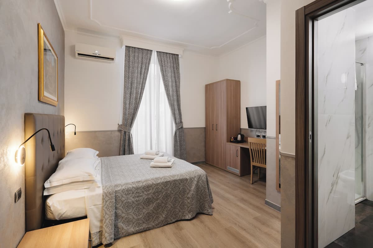 Habitación de hotel con cama, escritorio, armario y baño visible a través de una puerta abierta.