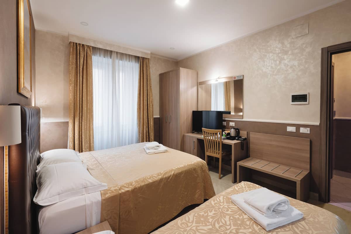 Habitación de hotel con dos camas, un escritorio, una silla, un televisor y un espejo.