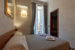 Una camera d'albergo con un letto, un comodino, una lampada a parete, una finestra con tende e un'uscita verso il bagno.