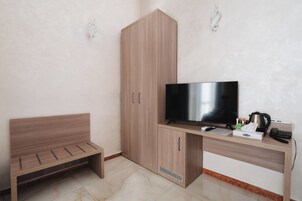 Una stanza con una panchina in legno, una TV, una scrivania con un bollitore e un telefono.