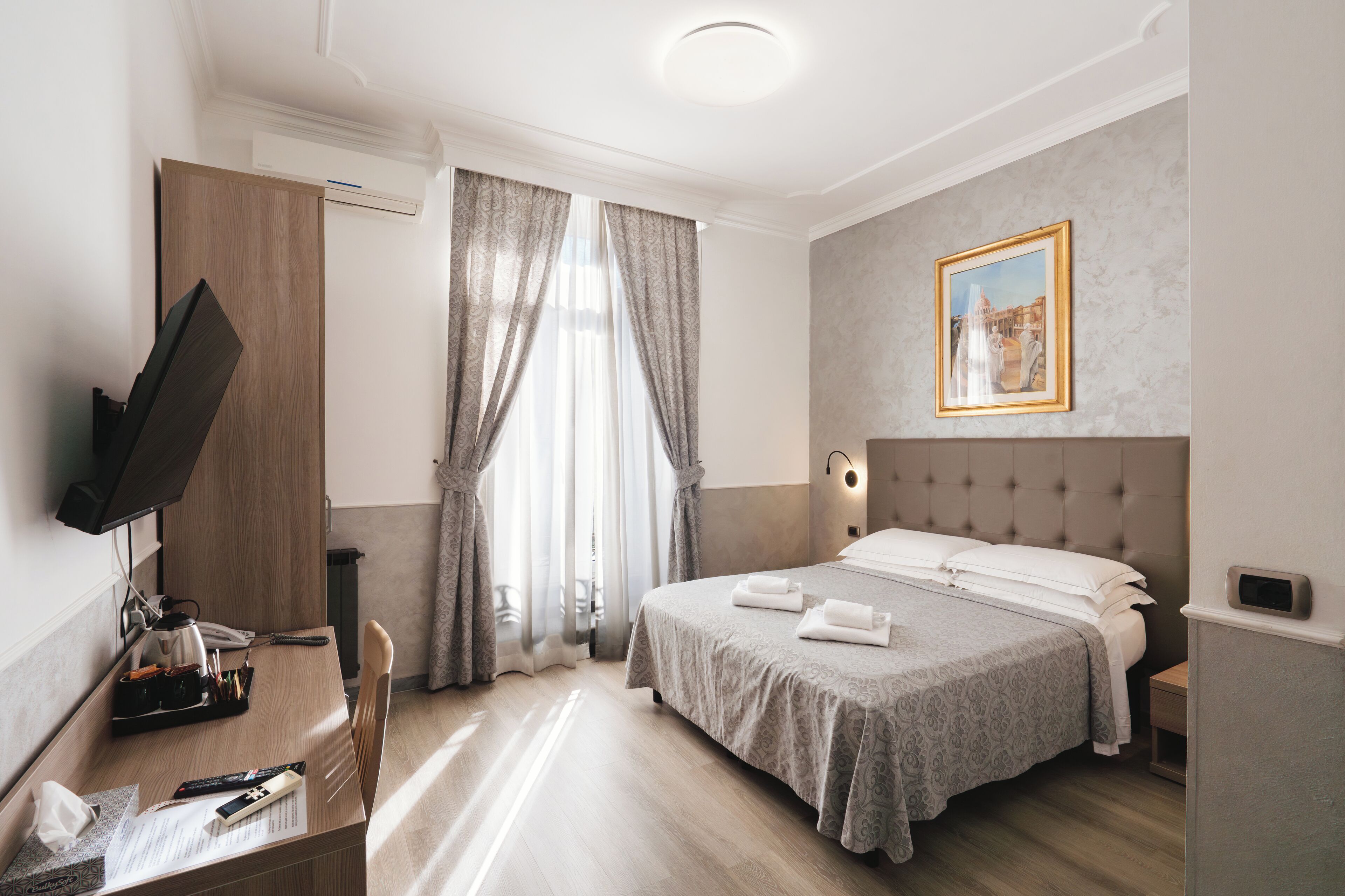Habitación de hotel con cama, escritorio con computadora, televisión y un cuadro en la pared.