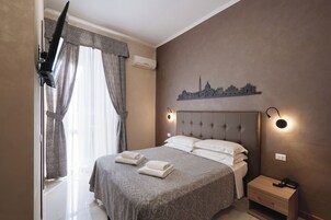 Una camera da letto con un letto, un comodino, una lampada a muro e una decorazione raffigurante un panorama cittadino.
