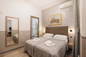 Camera d'albergo con due letti, un grande specchio, un quadro del Colosseo e un bagno visibile attraverso una porta aperta.