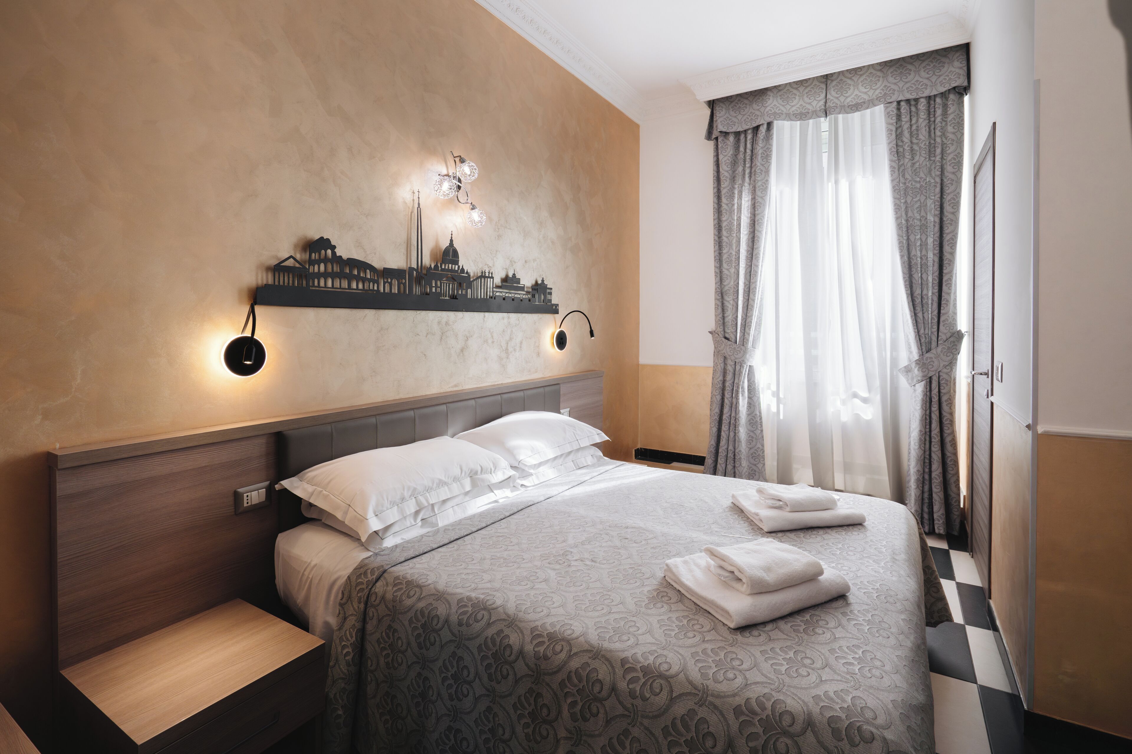 A neatly made bed with a patterned bedspread, a headboard with a cityscape light fixture, and a checkered floor.