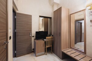 A compact room with a wooden desk, a chair, a television, and a wardrobe.
