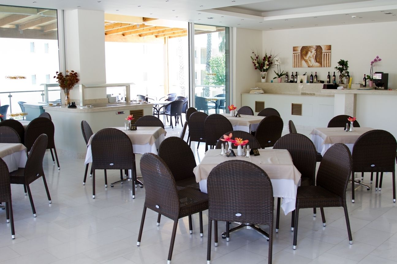 Un restaurante con sillas y mesas de mimbre, una barra con caja registradora y un amplio ventanal con vistas al exterior.
