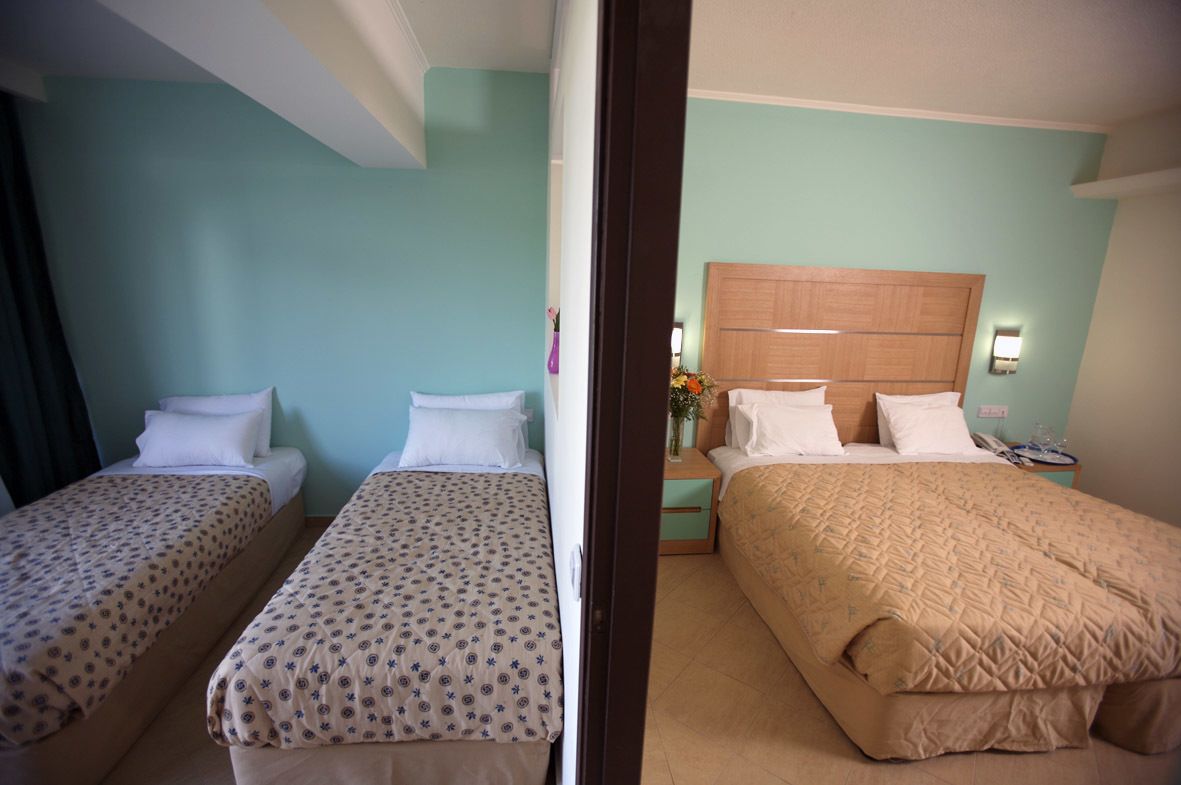 A hotel room with two single beds, a wooden headboard, a nightstand with a lamp, and a vase with flowers.
