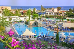 A resort pool area with multiple pools, lounge chairs, umbrellas, and a view of the sea. - Sun Palace Hotel - All inclusive (Rhodes)