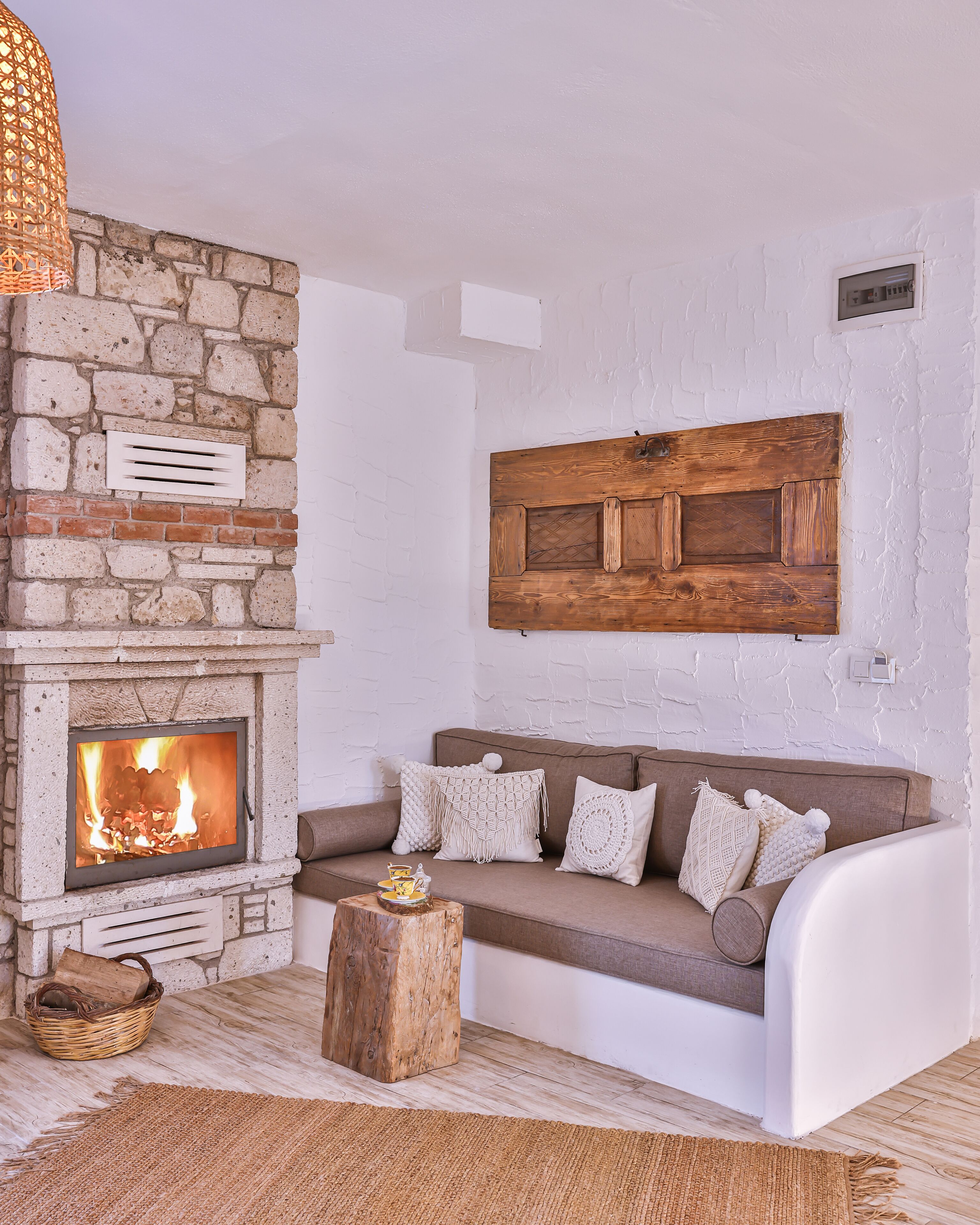 A cozy living room with a stone fireplace, a brown sofa with patterned cushions, and a woven rug.