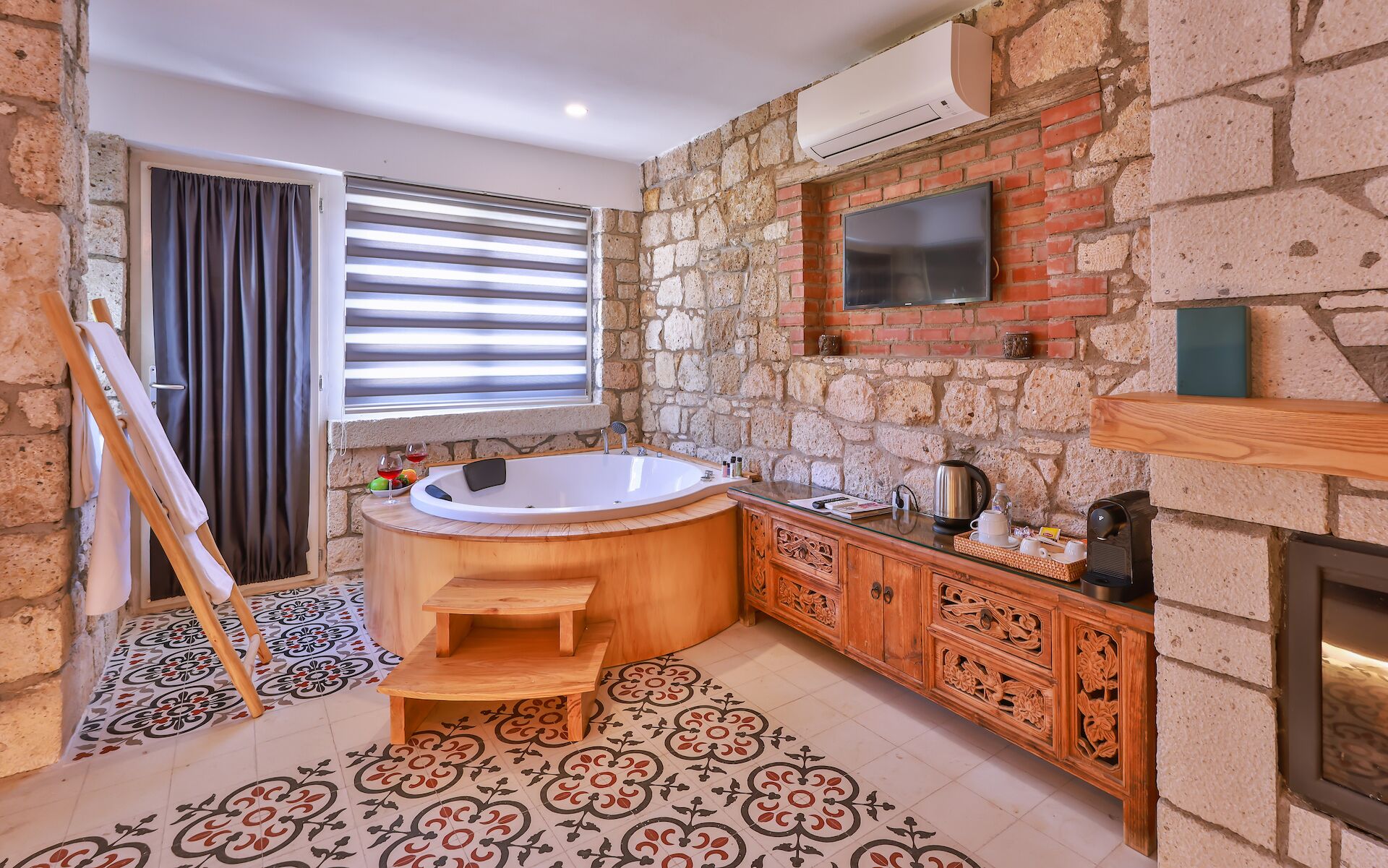 Un baño con pared de piedra, una bañera de madera, un tocador de madera y un televisor de pantalla plana sobre el espejo.