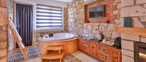 Un baño con pared de piedra, una bañera de madera, un tocador de madera y un televisor de pantalla plana sobre el espejo.