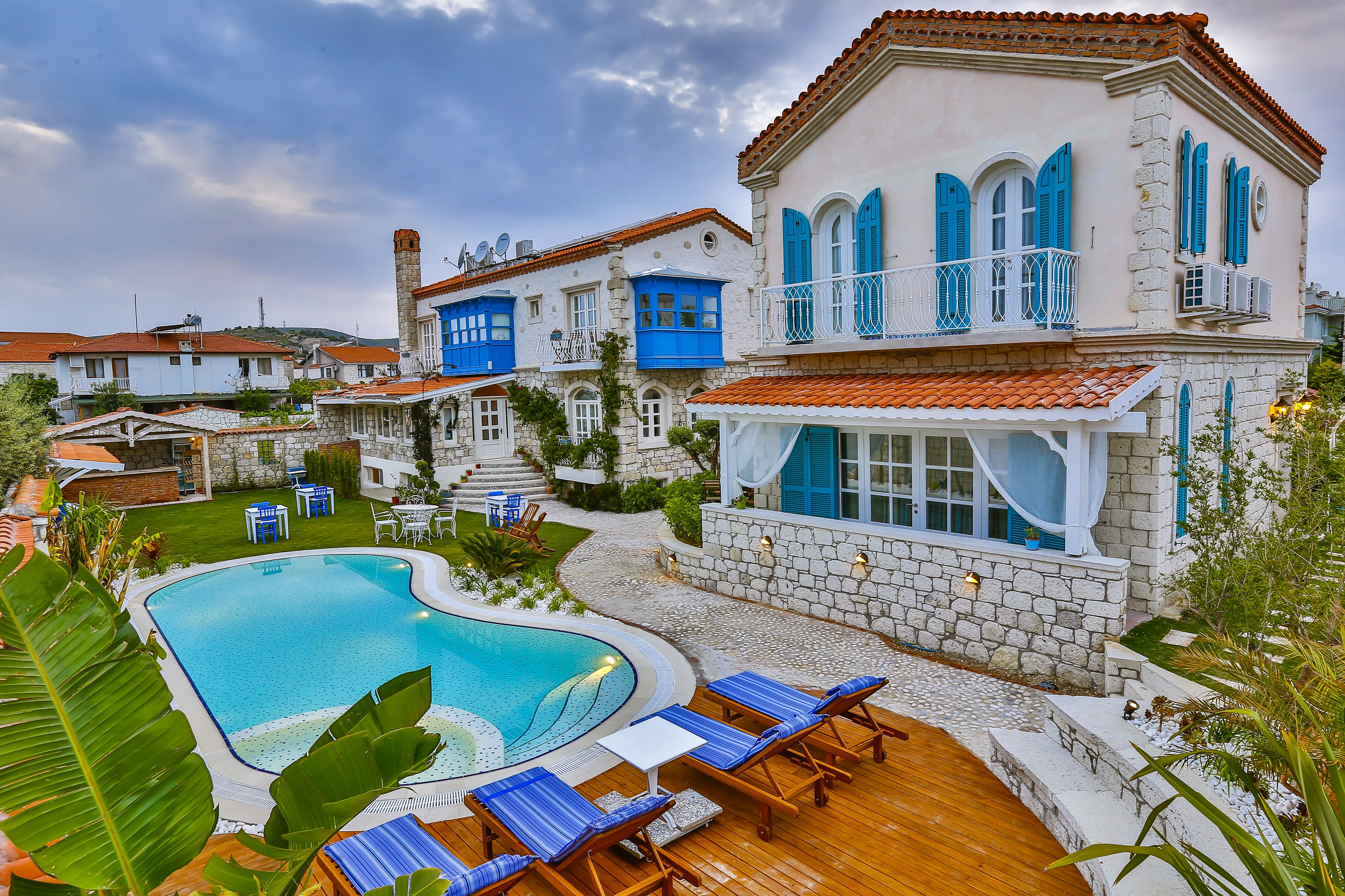 A pool area with lounge chairs, a stone wall, and a building with blue shutters.