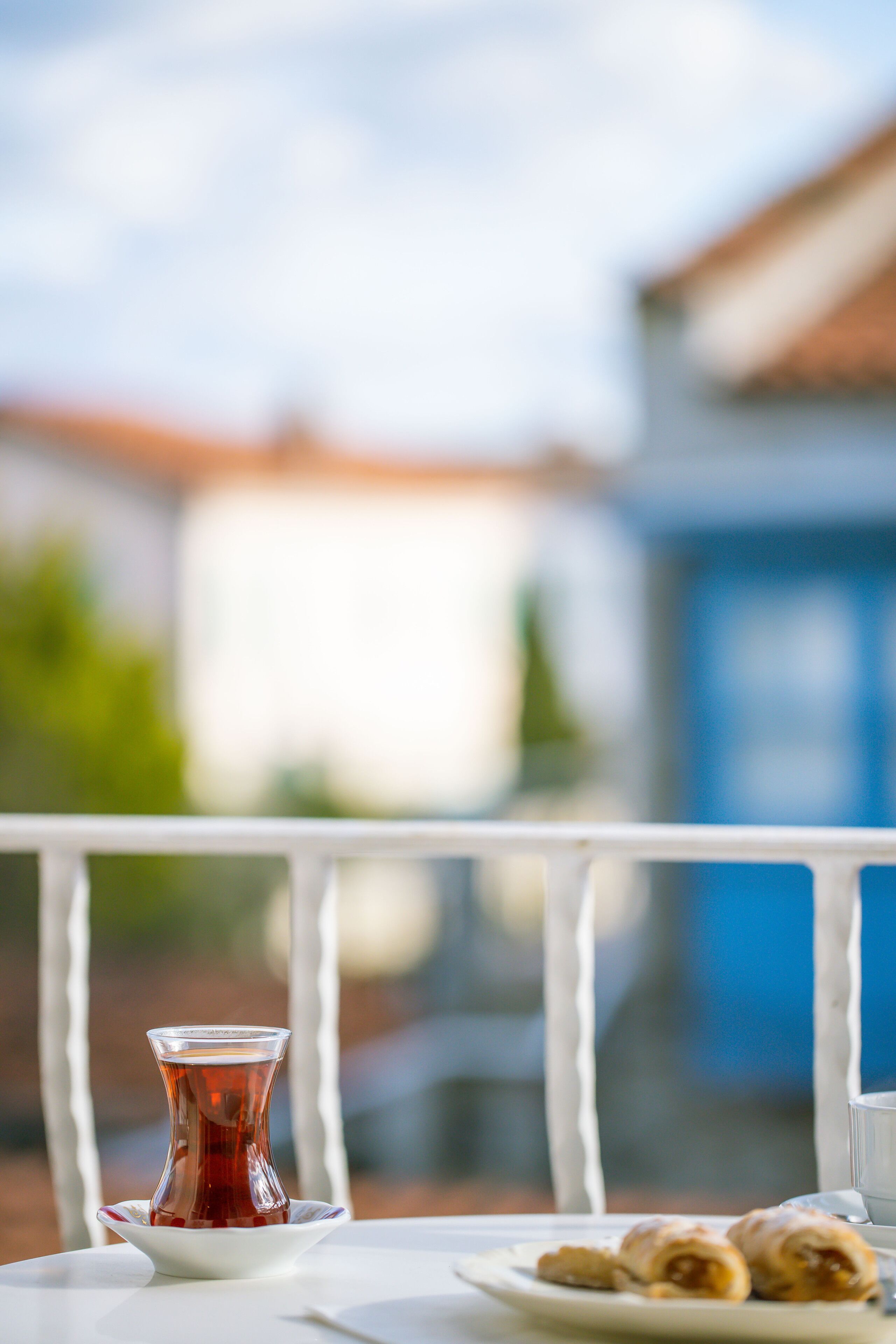 A table with a glass of tea and pastries on a balcony with a railing.