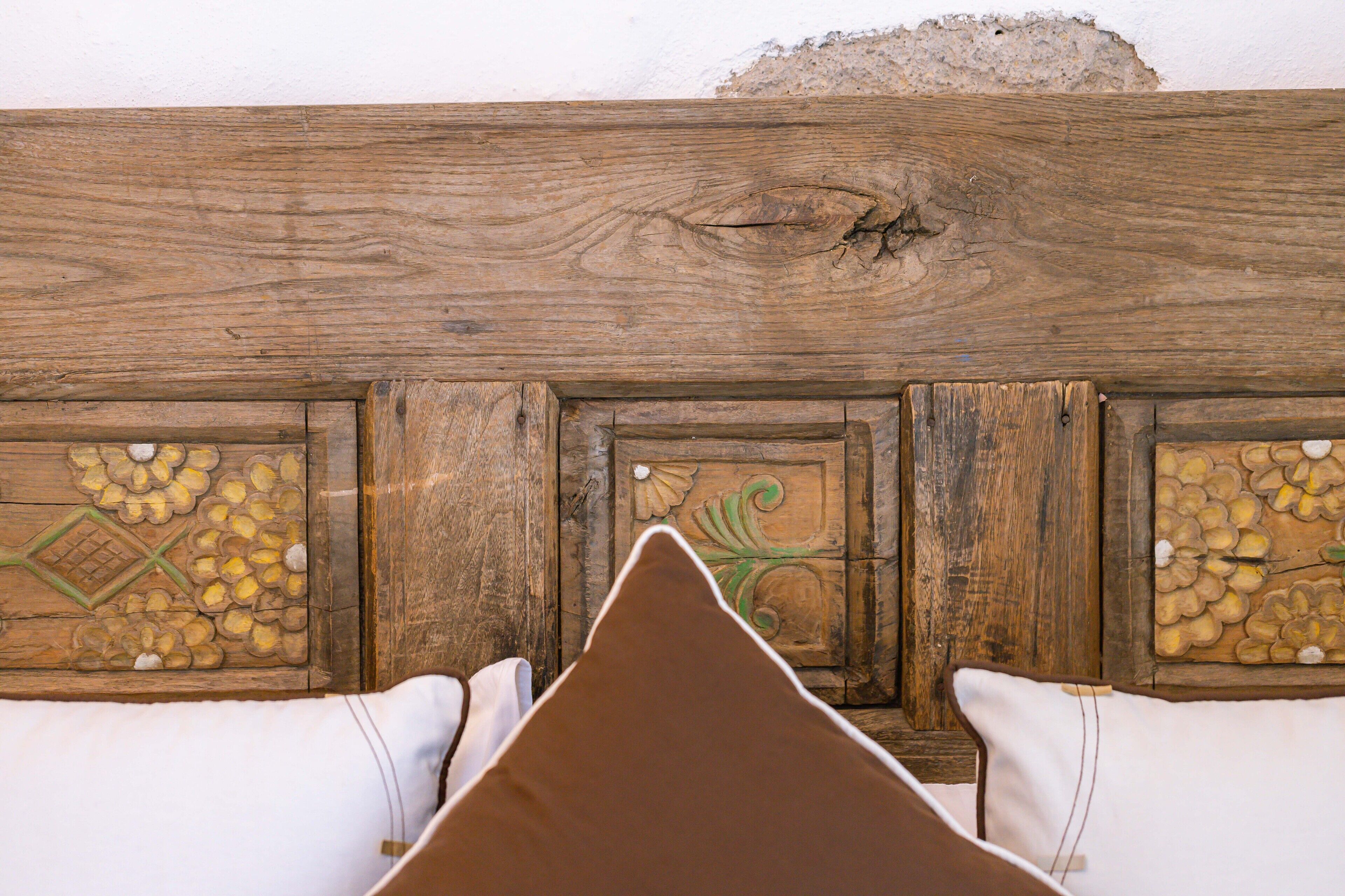 A wooden headboard with floral carvings and a brown pillow in front.