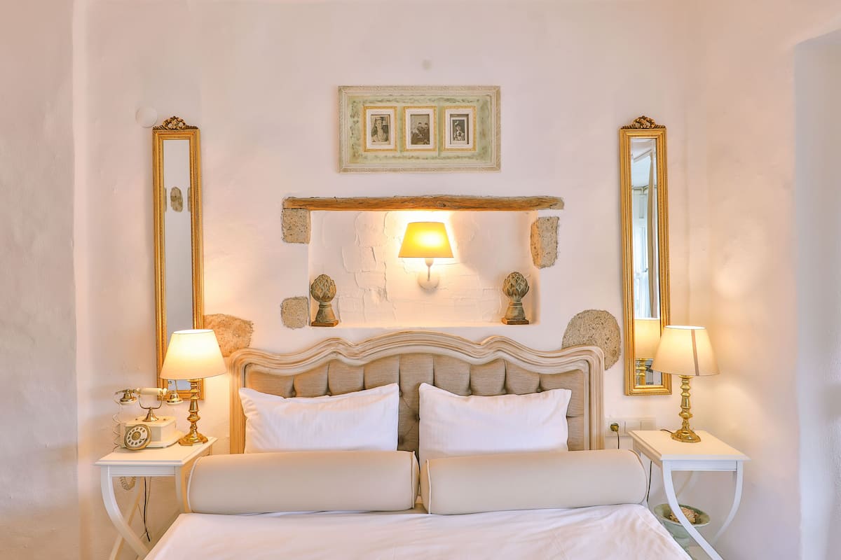 A neatly made bed with two pillows, a bedside table with a lamp, and two wall-mounted mirrors.