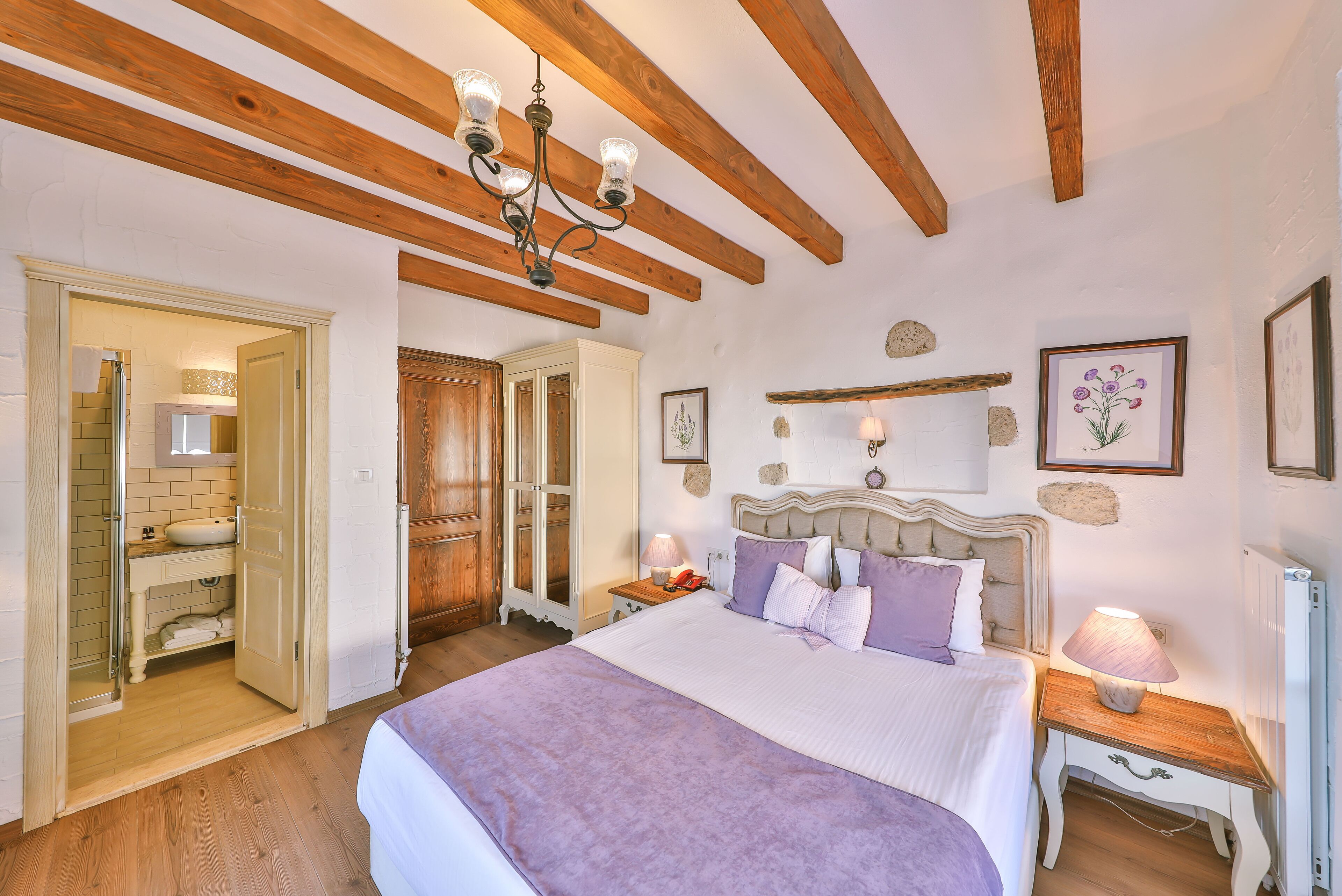 A bedroom with a large bed, wooden beams, a chandelier, a nightstand, and a bedside table.