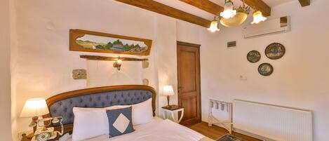 A bedroom with a bed, wooden beams, a painting, a radiator, and a telephone on a nightstand.